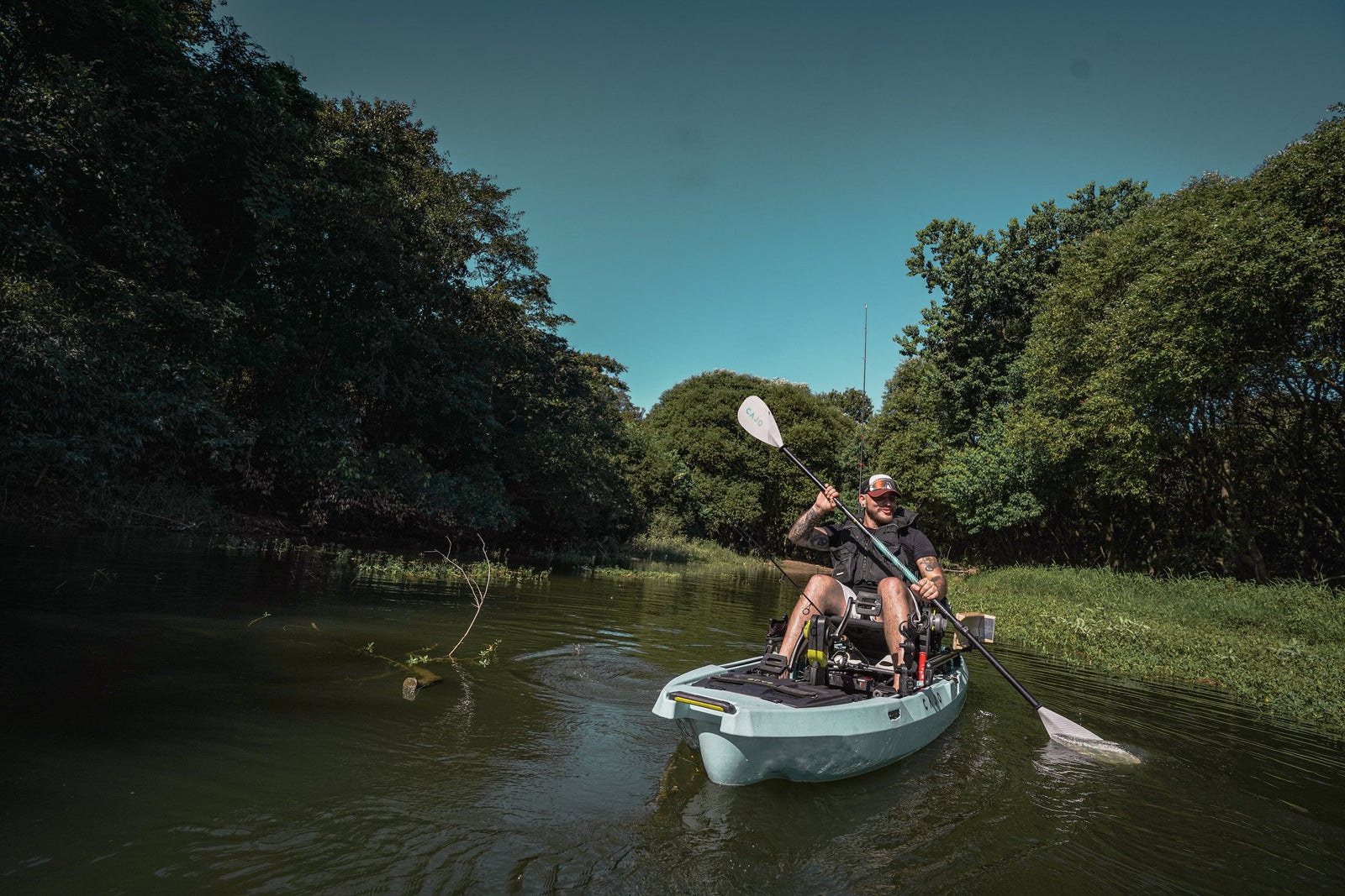 An angler paddling a sit-on-top fishing kayak down a quiet river