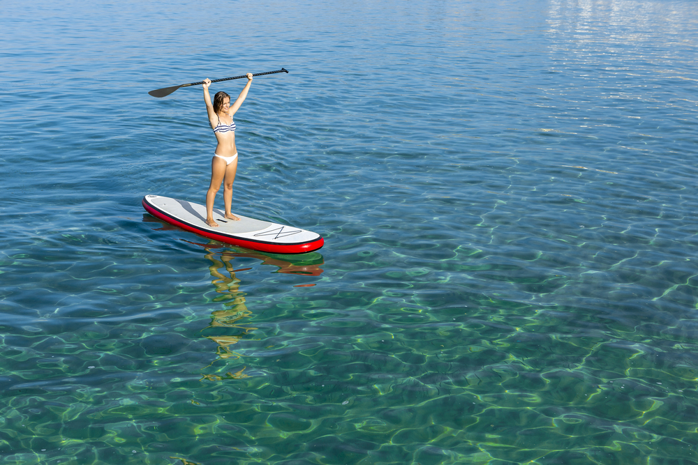 žena so zdvihnutými rukami a učí sa paddle-surfovať